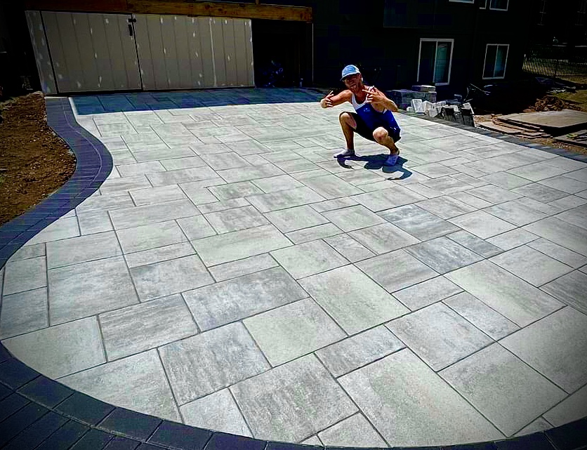 A white male crouching on a patio made of pavers.
