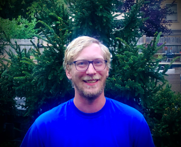 A white male with blond hair and a blond beard, glasses, and wearing a blue shirt.