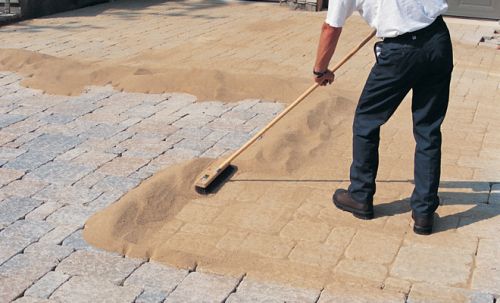 Man spreading polymeric sand on a paver installation.
