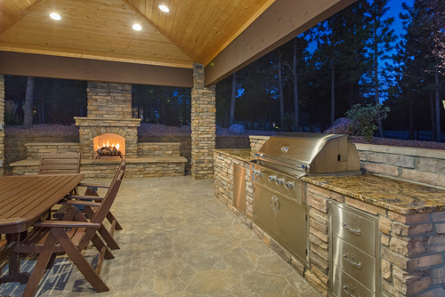 outdoor ditchen with roof, fireplace with fire, table and chairs, storage and grill.