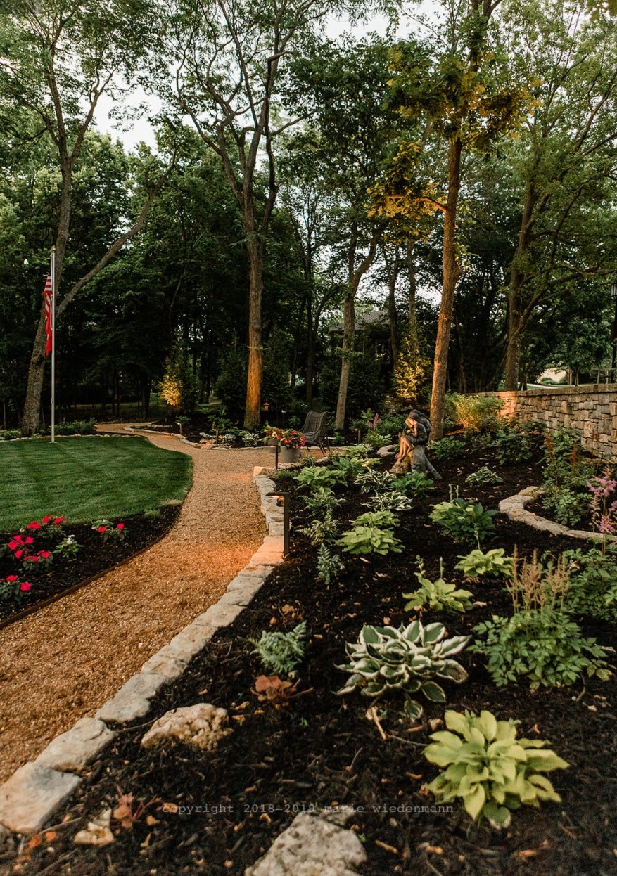 a garden path and landscape bed with plants in it.