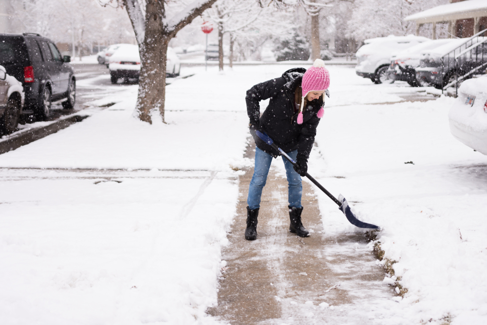 person in pink hat shoveling snow off a sidewalk