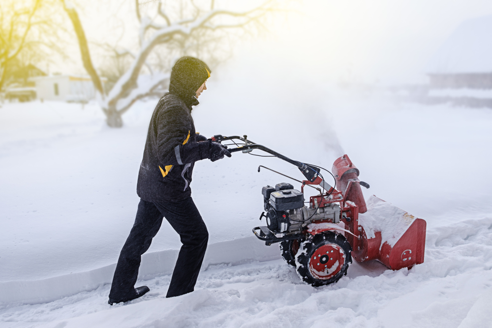 person pushing a snowblower to clear sidewalk of snow