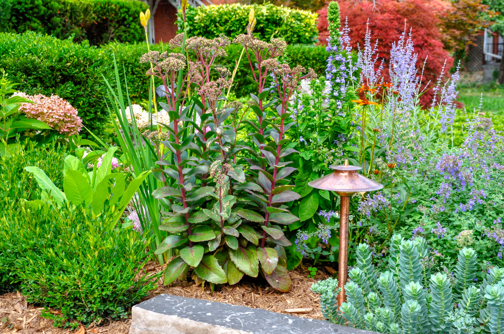 A copper outdoor light in a landscape bed full of flowers.