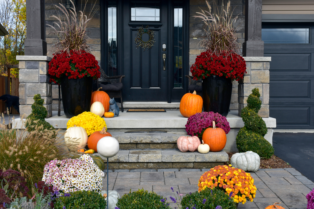 A porch decorated with planters with colorful flowers in them and pumpkins of several colors.