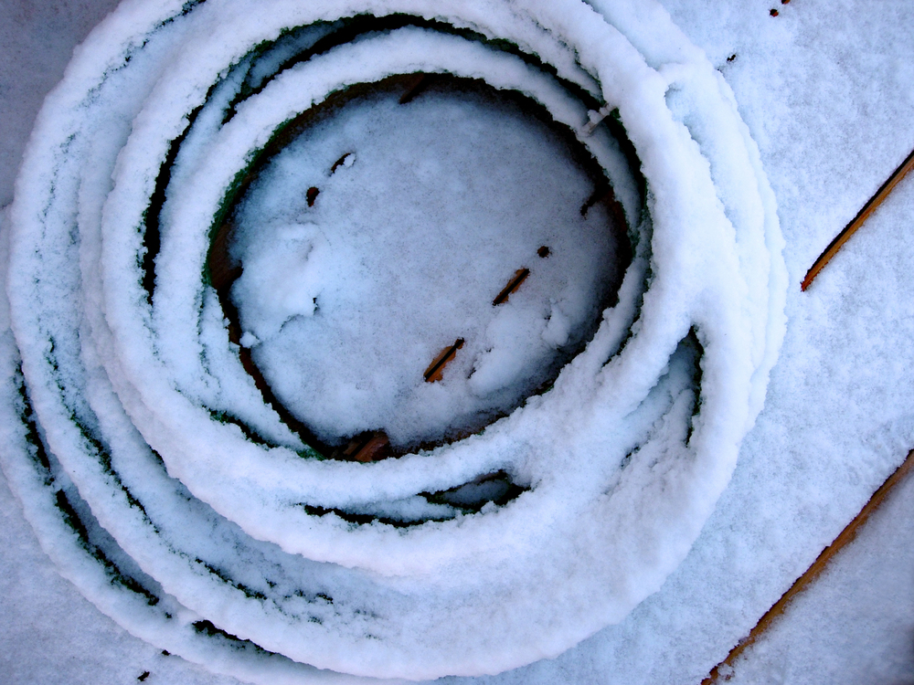 A snow covered water hose on a deck.