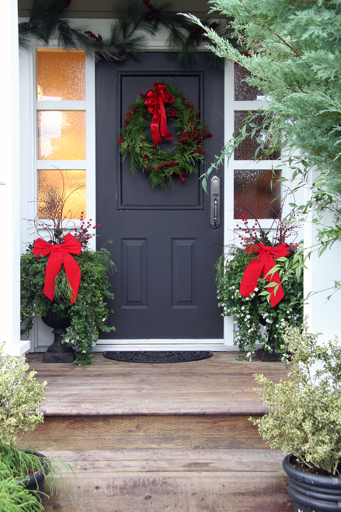A door with a Christmas wreath on it and two Christmas planters.