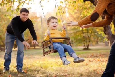 Man pushing youing boy in a swing while someone watches.
